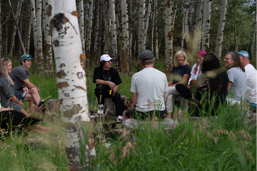 A group sitting in a circle in the grass among white-barked aspens
