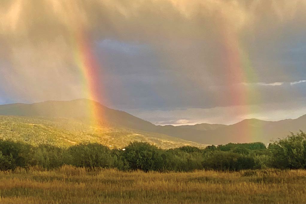 A double rainbow arcing over green foothills above an open field
