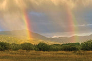 A double rainbow arcing over green foothills above an open field