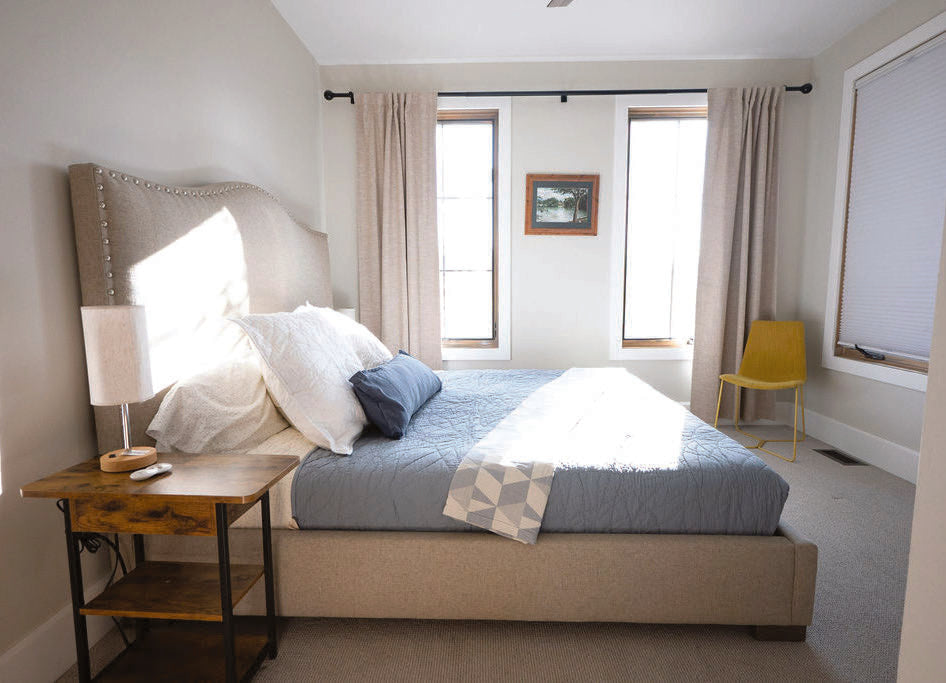 A guest bedroom with a king bed and tall windows letting in morning light