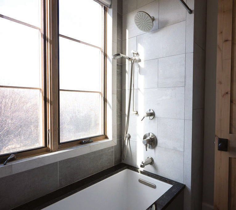 A guest bathroom with a soaking tub and rain shower beside a bank of windows