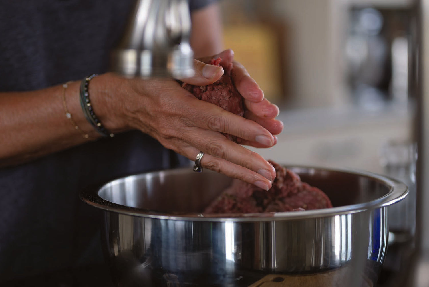 Hands shaping a patty of ground meat over a mixing bowl in the kitchen