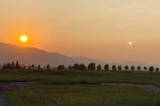 Hazy sun setting behind the mountains above an open meadow